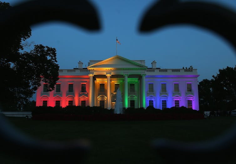 The White House is shown at night, light up with rainbow colors.