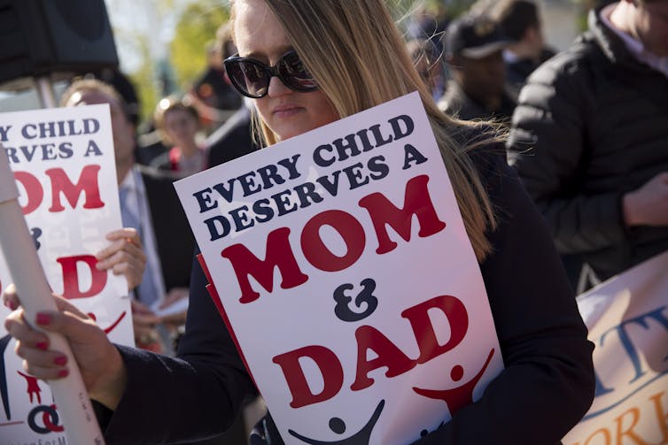 A woman holds up a sign that says 'every child deserves a mom and dad'