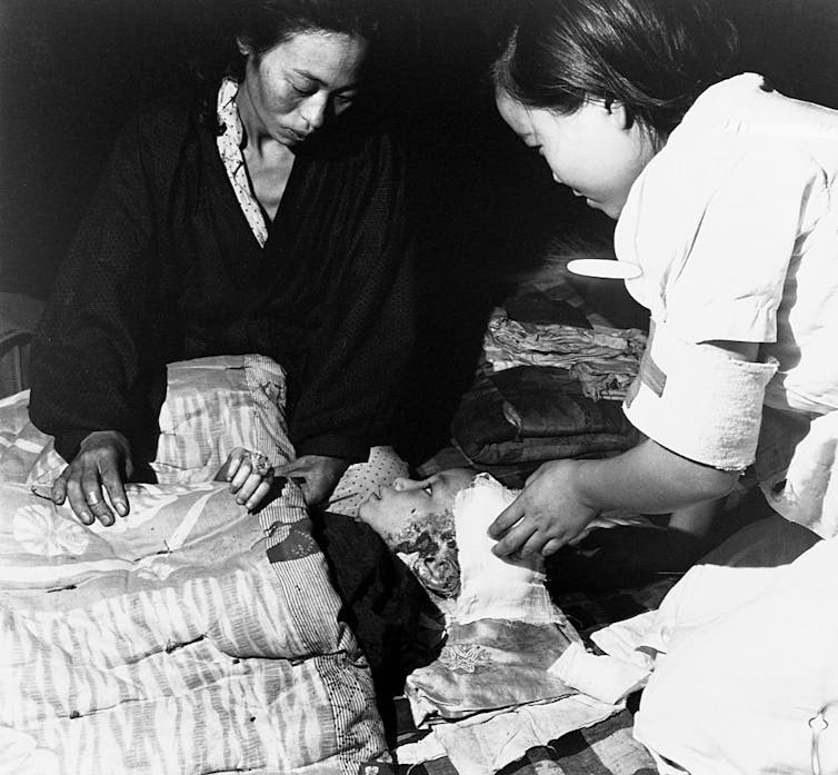 Two women kneel as they tend to a child injured by the atomic bomb in Hiroshima.