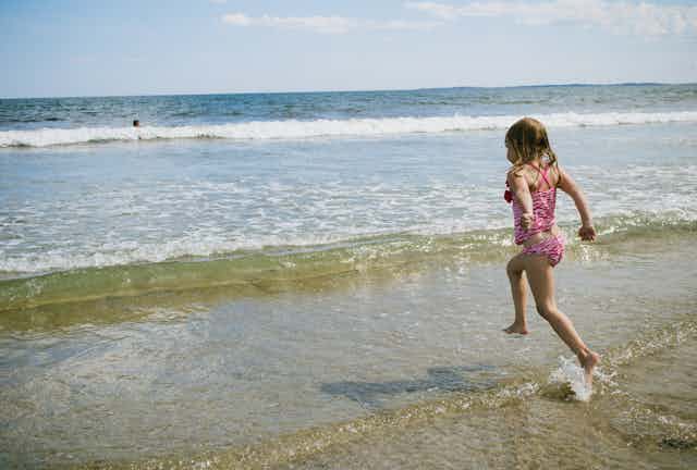 Una niña en bañador corre hacia las olas desde la orilla.
