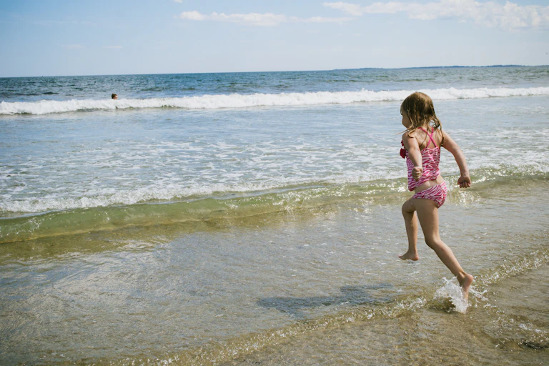 Una niña en bañador corre hacia las olas desde la orilla.