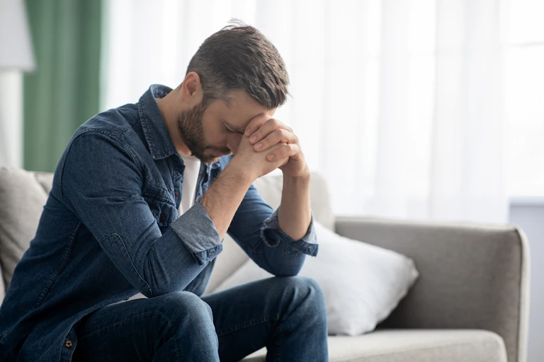 Middle aged man sits on sofa with head in his hands