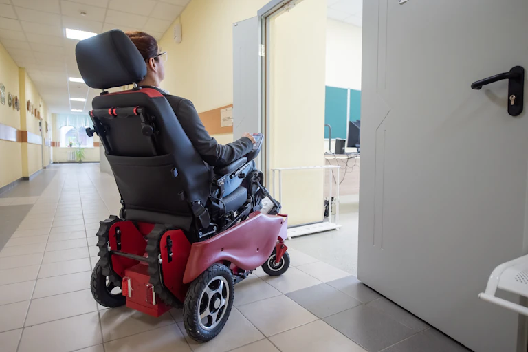 Una persona en silla de ruedas eléctrica entrando en un aula.