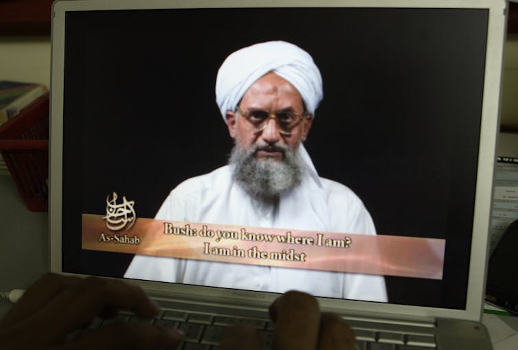 A laptop screen shows Ayman al-Zawahri speaking with the English translation below reading 'Bush do you know where I am. I am in the midst.'