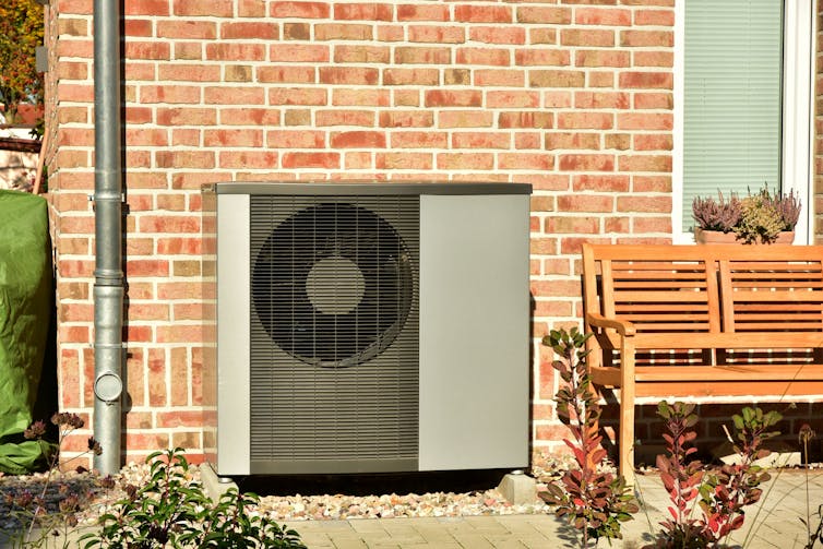 A large grey air conditioner unit attached to the brick exterior of a house.
