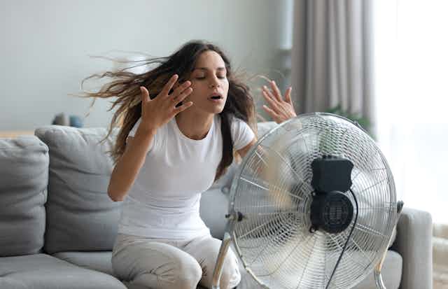 Una mujer sentada en un sofá recibe aire de un ventilador.