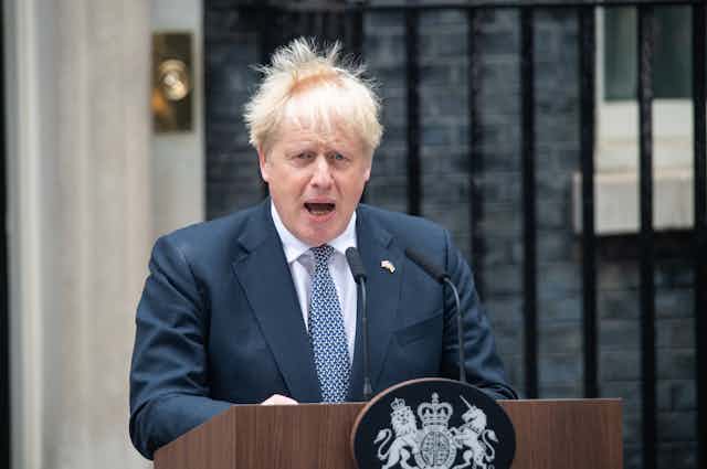 Boris Johnson speaks at a podium in front of Downing Street, with his hair blowing wildly