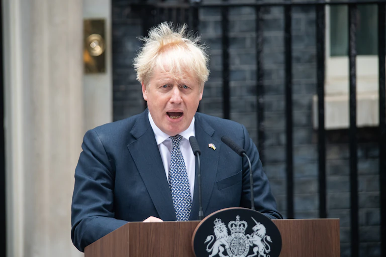 Boris Johnson speaks at a podium in front of Downing Street, with his hair blowing wildly
