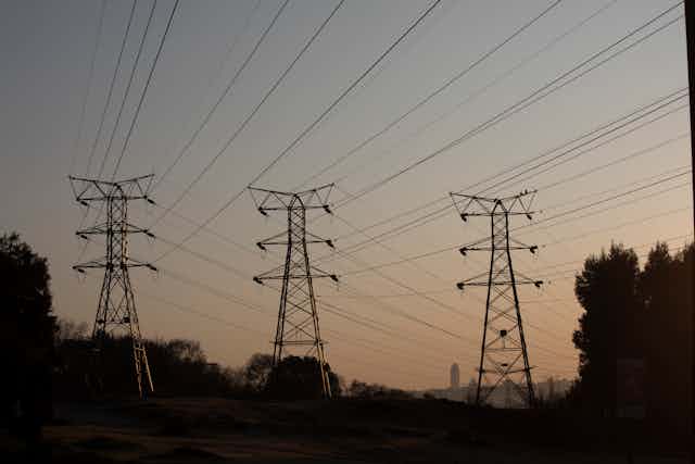 Three huge steel power pylons support several electricity cables over land. 