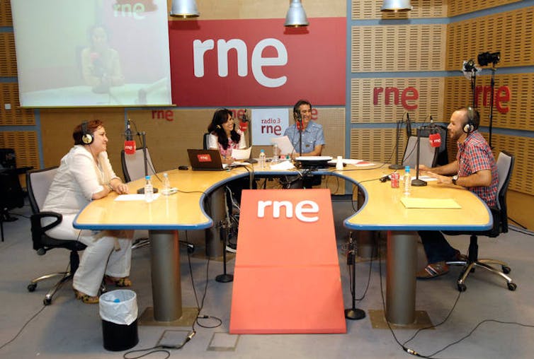 Cuatro personas están sentadas en una mesa de un estudio de radio, delante de los micrófonos, para realizar un programa.