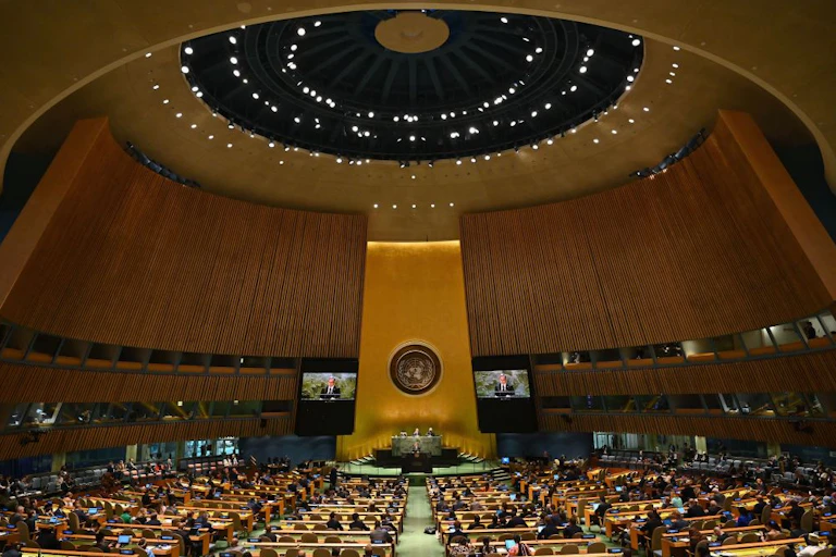 A huge meeting room with a tall ceiling and gold-colored podium.