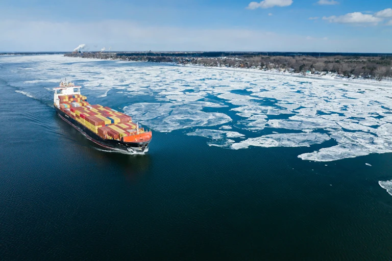 A full container ship travels on a partially frozen body of water