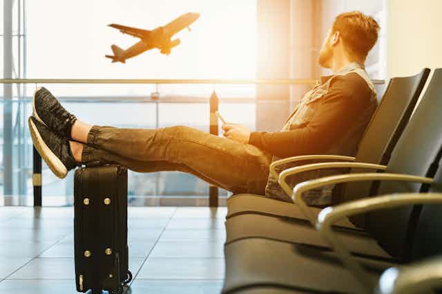 Man sitting on a chair in the airport with his feet on luggage
