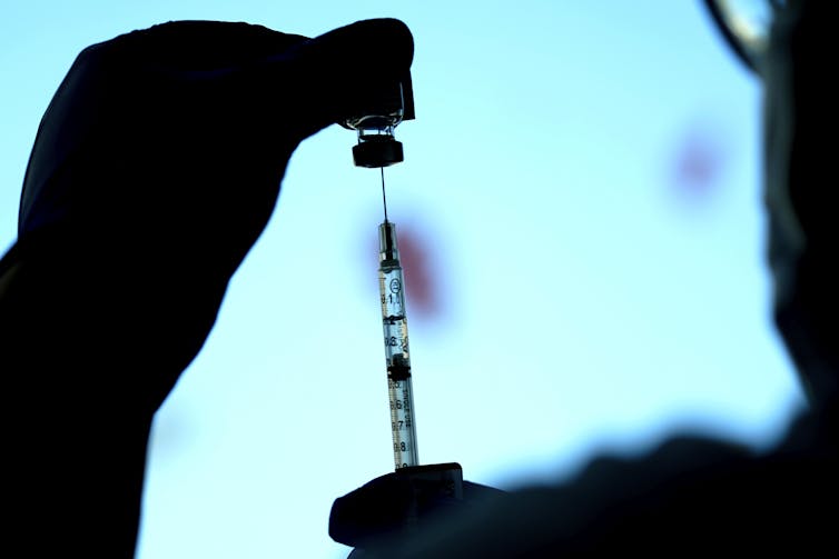 A dose of vaccine is seen in silhouette against a blue background.