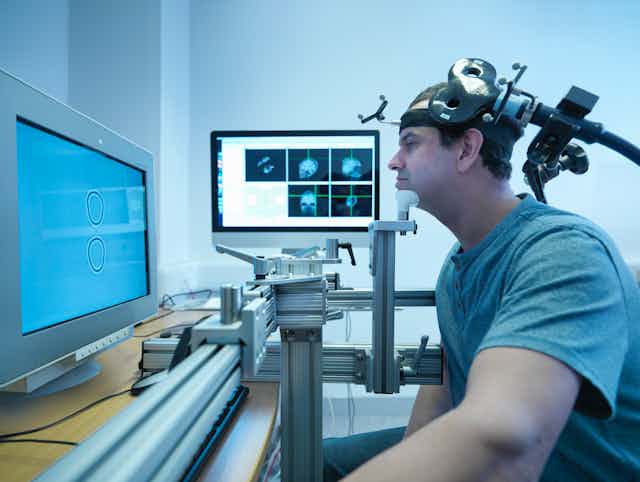 A man wearing a transcranial magnetic stimulation device, which is shaped like a Figure 8, is receiving a treatment.
