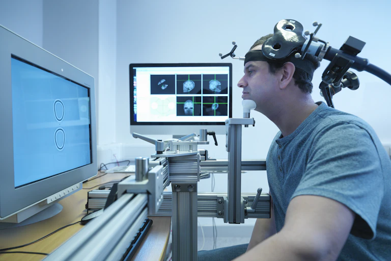 A man wearing a transcranial magnetic stimulation device, which is shaped like a Figure 8, is receiving a treatment.