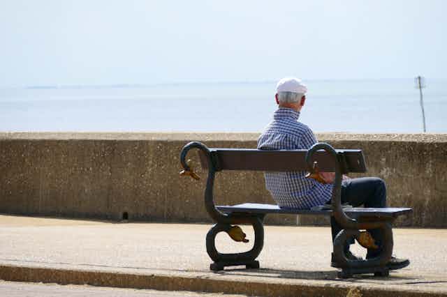 older man sits on bench by the sea