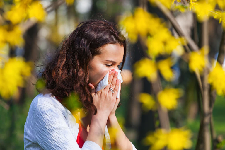 A woman blows her nose. She is outdoors.