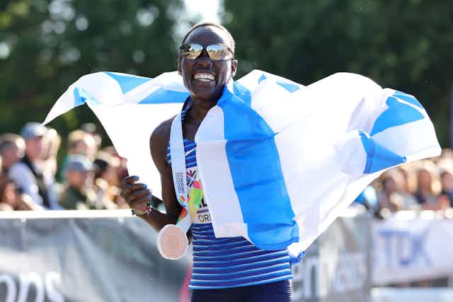 Victoious runner draped in a flag smiles at the camera