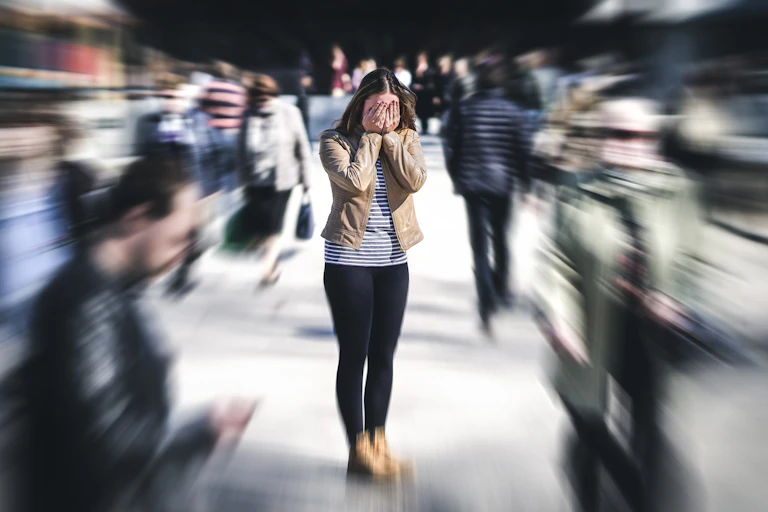 A woman stands with her face in her hands, surrounded by people who are blurred out