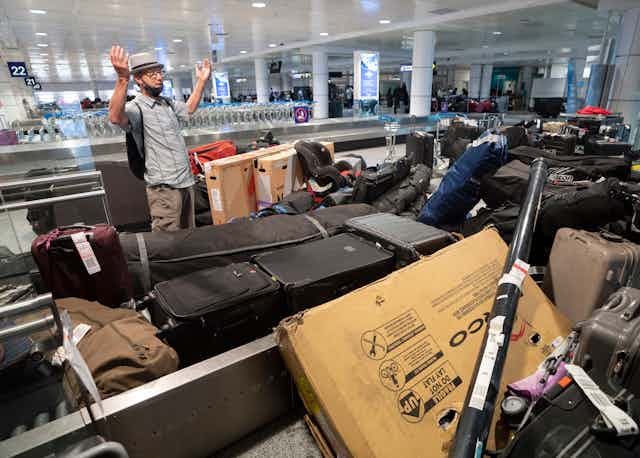 homme avec les bras levés devant une pile de bagages à l'aéroport
