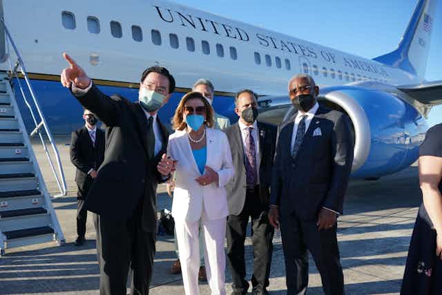 5 masked adults are shown standing together in formal clothing outside the US government airplane on a tarmac.
