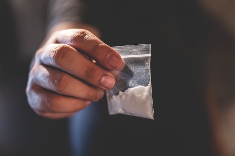 A hand holds a packet of a powdered drug.
