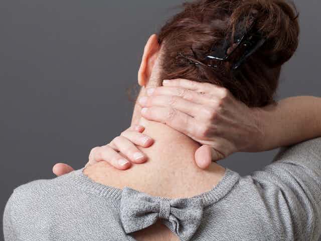 back of woman's upper body, leaning head and massaging neck with hands