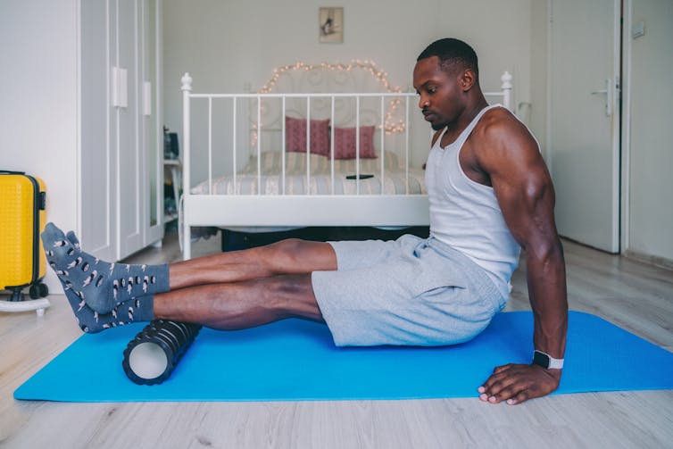 man seated on the floor with legs outstretched leans calf on foam roller