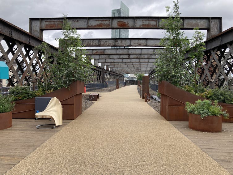 Seats, planted beds and a light coloured pathway on a bridge.