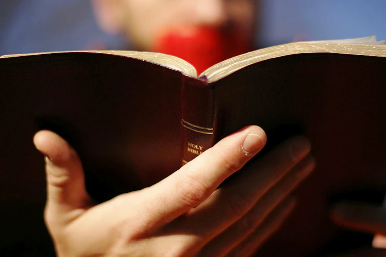 A close-up photo of a Bible held by a person with red duct tape over their mouth.
