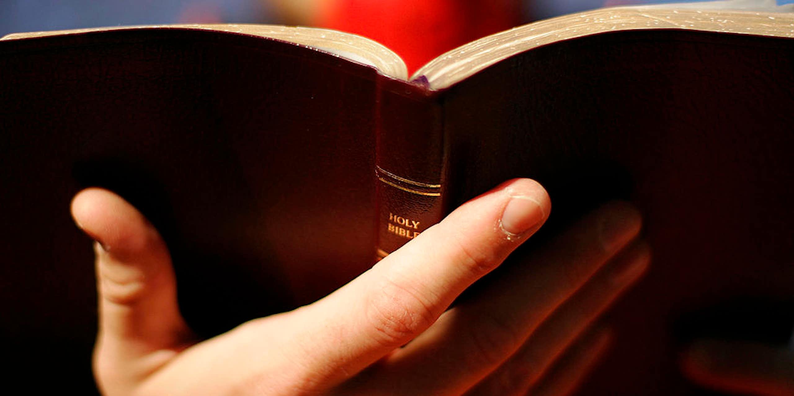 A close-up photo of a Bible held by a person with red duct tape over their mouth.