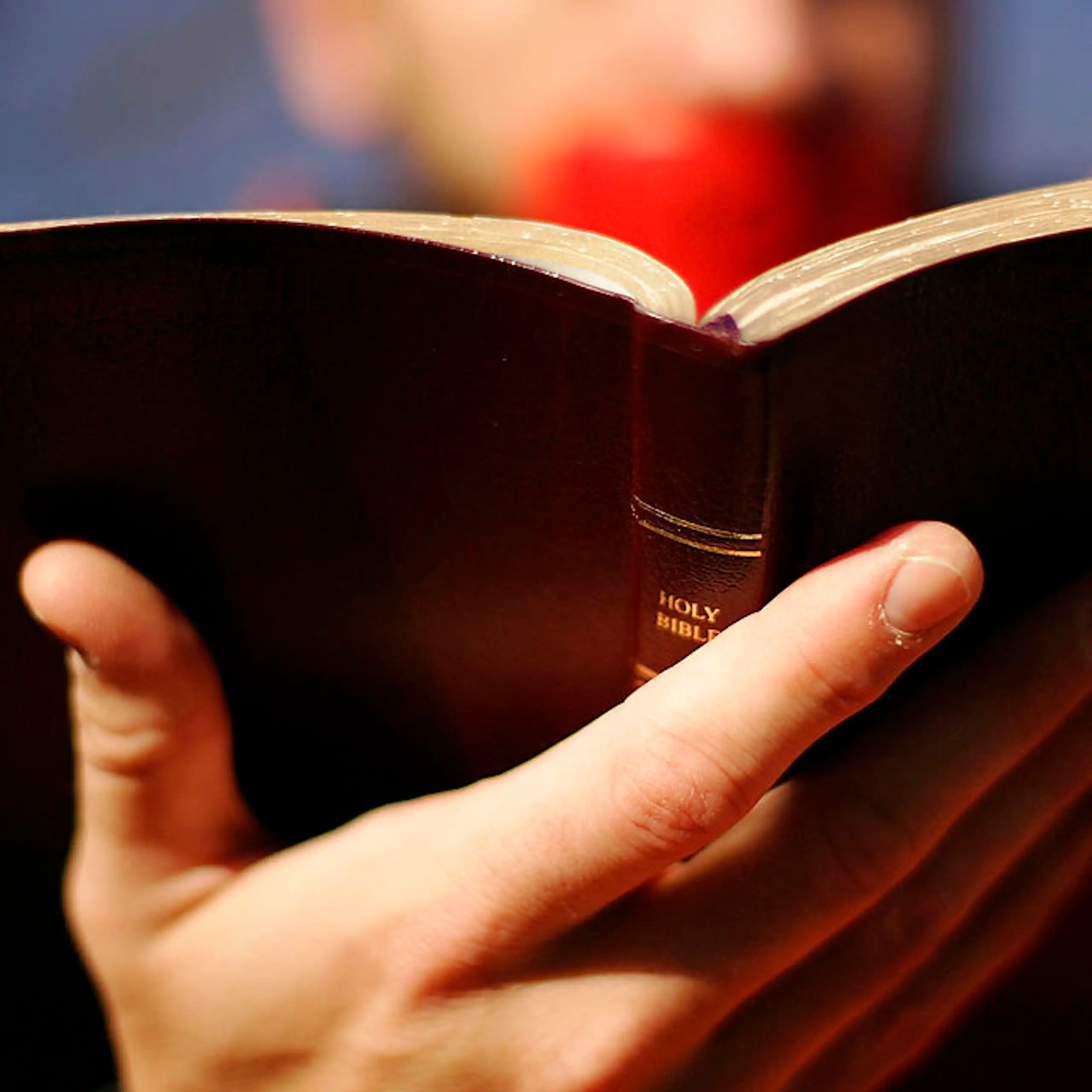 A close-up photo of a Bible held by a person with red duct tape over their mouth.
