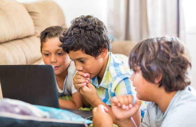 Three young Aboriginal kids look at a laptop.