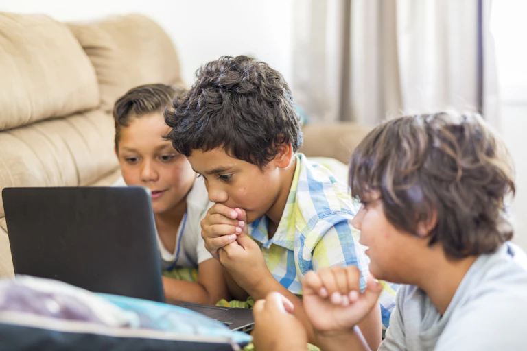 Three young Aboriginal kids look at a laptop.