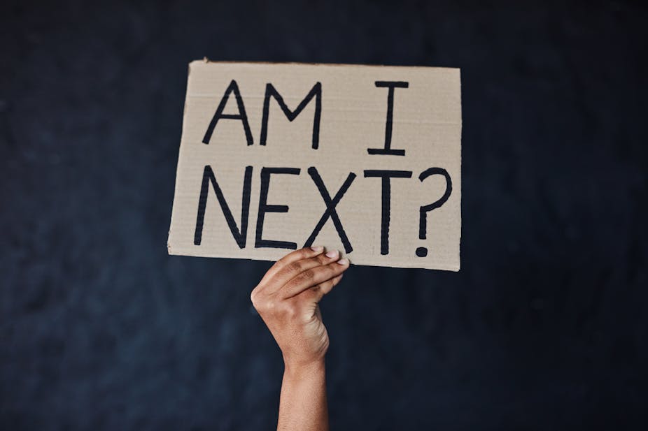 A woman's hand carries a placard asking: 'Am I next'.