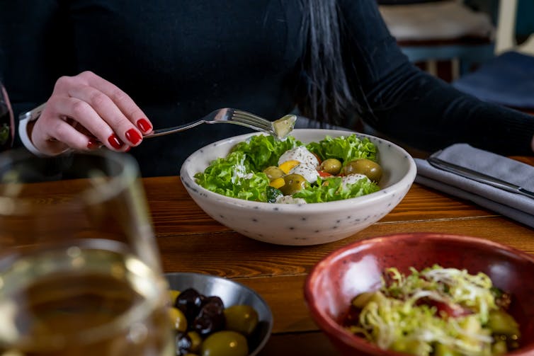 A diner enjoys a Greek salad with a glass of white wine.