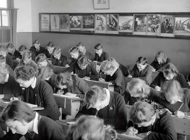 Una clase de alumnos uniformados se inclina sobre sus pupitres mientras hace un examen.