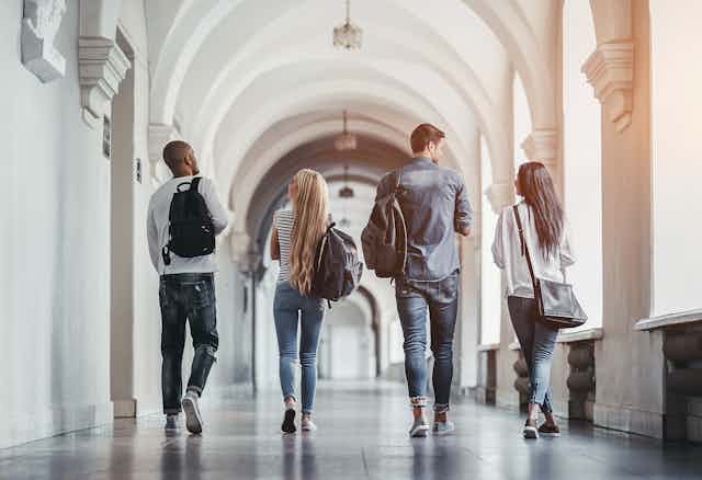 View from behind of four students walking side by side down a university hallway