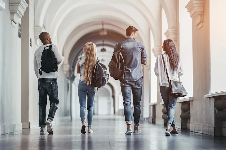View from behind of four students walking side by side down a university hallway