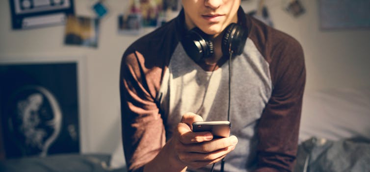 A young man sitting on his bed looking down at a mobile phone