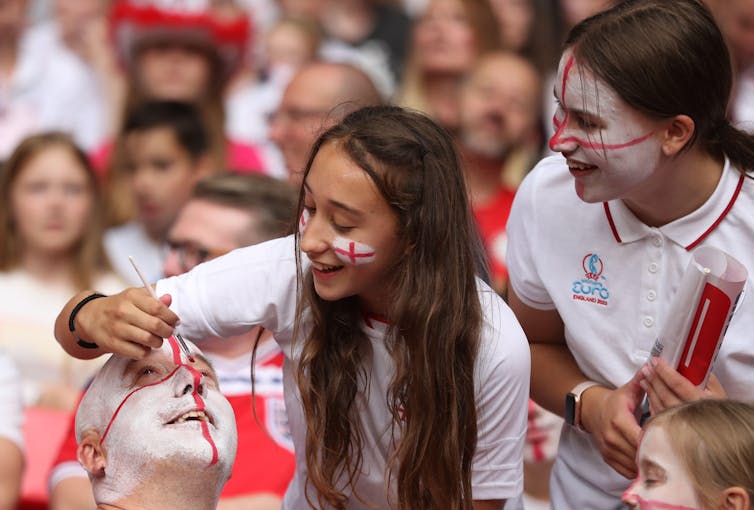 A man has his face painted with English flag by girls.