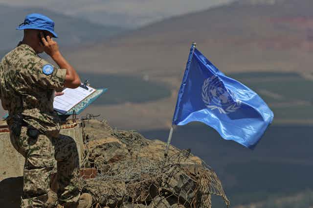 Man in military camouflage on phone next to blue flag