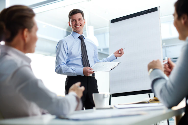 A man in a tie holds a clipboard and points, smiling confidently, to a blank poster
