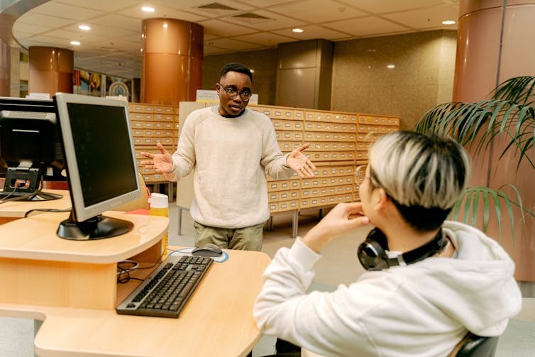 Two people seen talking in a library.