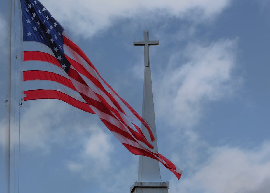 An American flag flies on a flagpole in front of a church steeple.