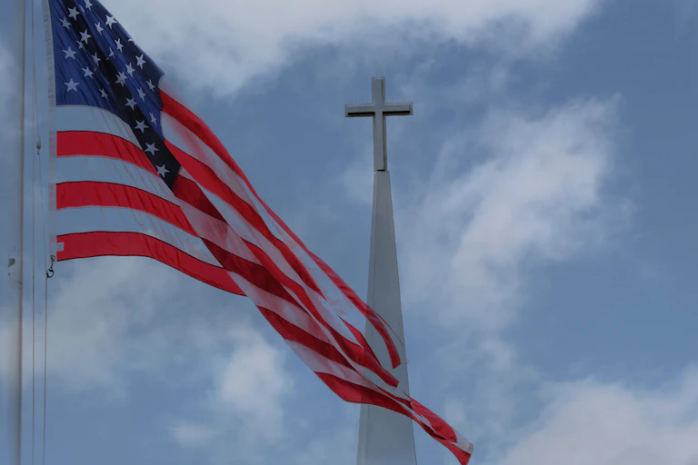 An American flag flies on a flagpole in front of a church steeple.