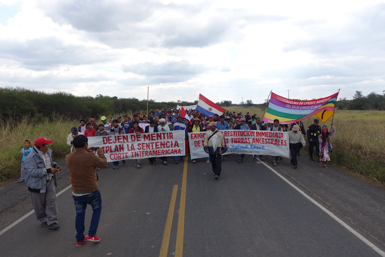 People walk down a highway carrying banners demanding the state return their ancestral lands.