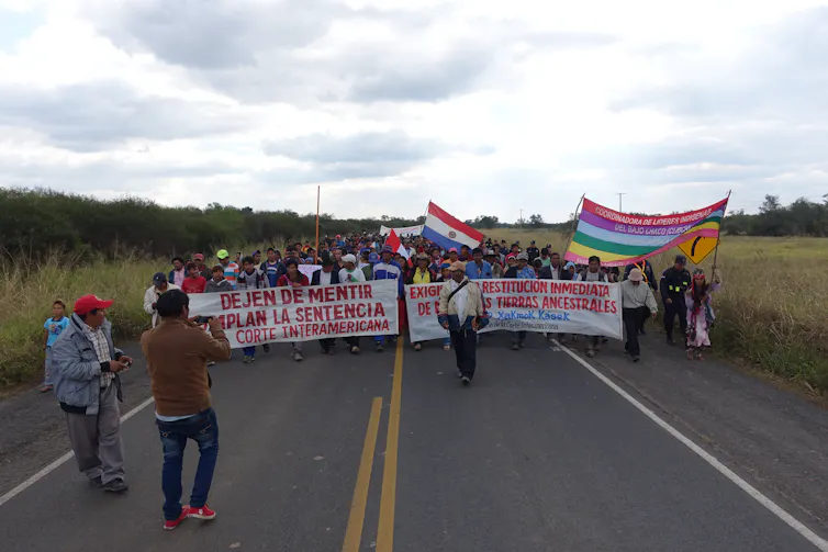 People walk down a highway carrying banners demanding the state return their ancestral lands.