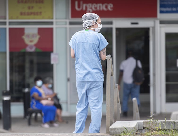 A woman in scrubs standing in front of the entrance to a hospital